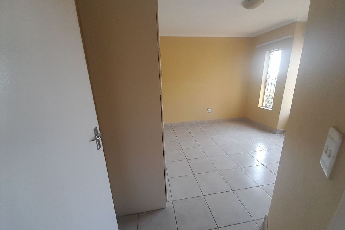 A bright, empty bedroom featuring neutral tiled flooring, a built-in cupboard, and natural light from the window.