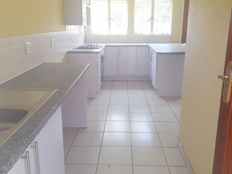 A functional, empty kitchen featuring white cabinetry, laminate countertops, tiled flooring, and a built-in hob, offering a clean canvas for updates.