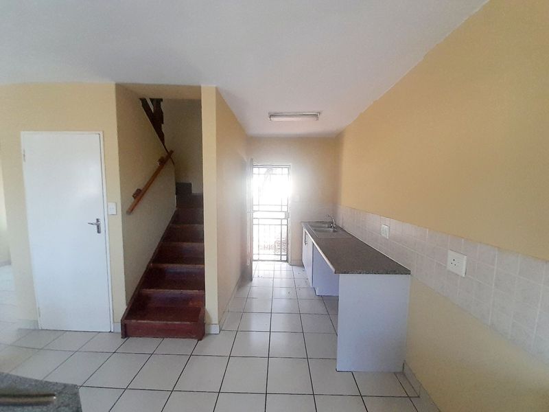 An empty kitchen area featuring tiled flooring, built-in cabinetry with a sink, and an adjacent staircase leading to the upper level.
