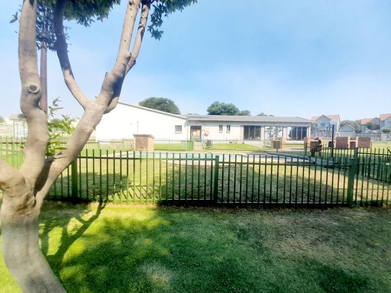 Communal pool area featuring a swimming pool, metal safety fencing, and a brick braai facility set within a grassed garden space.
