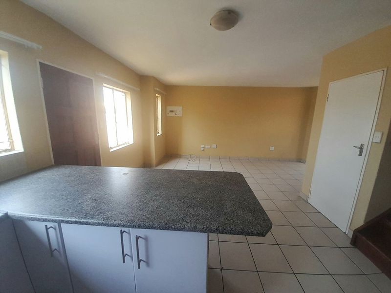 An open-plan living and kitchen area featuring tiled flooring, a kitchen island with a laminate countertop, and neutral wall finishes.