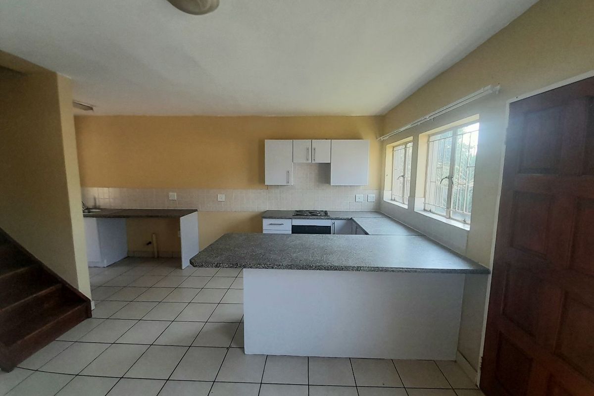 An empty kitchen featuring built-in cabinetry, laminate countertops, a hob, and an oven, with tiled flooring and security bars on the windows.