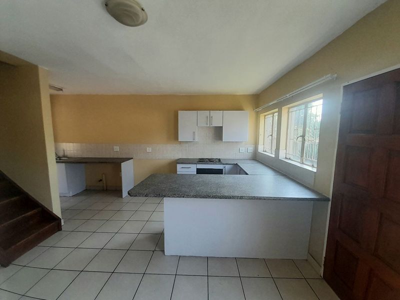 An empty kitchen featuring built-in cabinetry, laminate countertops, a hob, and an oven, with tiled flooring and security bars on the windows.