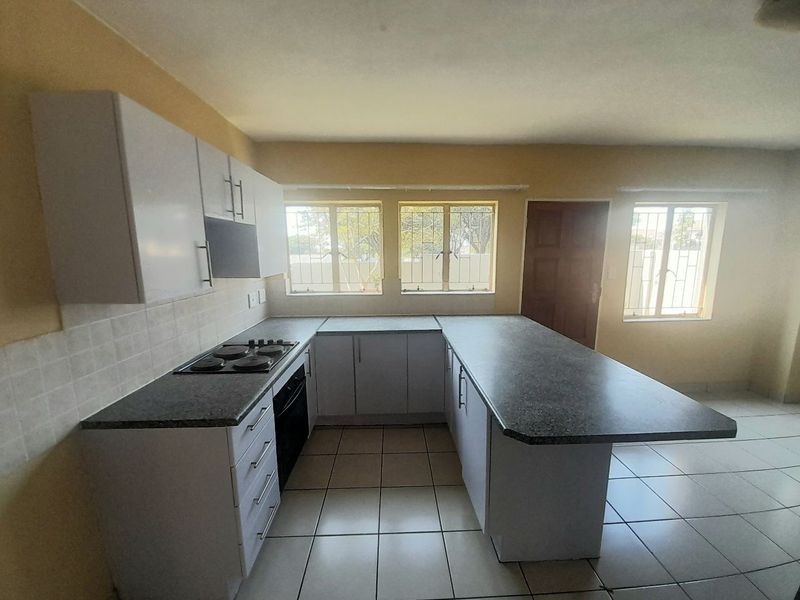 A functional kitchen featuring white cabinetry, dark laminate countertops, an integrated electric hob and oven, and tiled flooring with security bars on the windows.