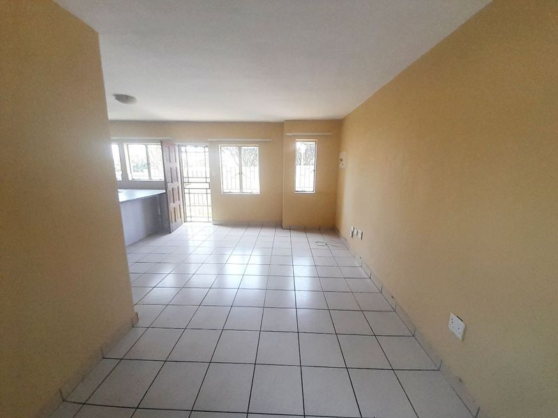 An open-plan living and kitchen area featuring neutral wall paint, ceramic floor tiles, and security fixtures on windows and doors.