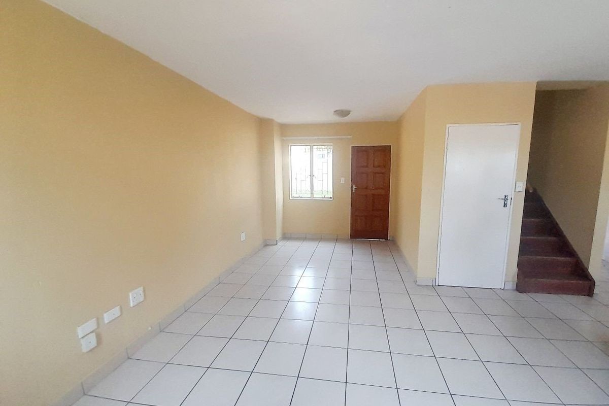 An empty, open-plan living area featuring neutral tiled flooring, a staircase, and a security gate, offering a blank canvas for personalization.