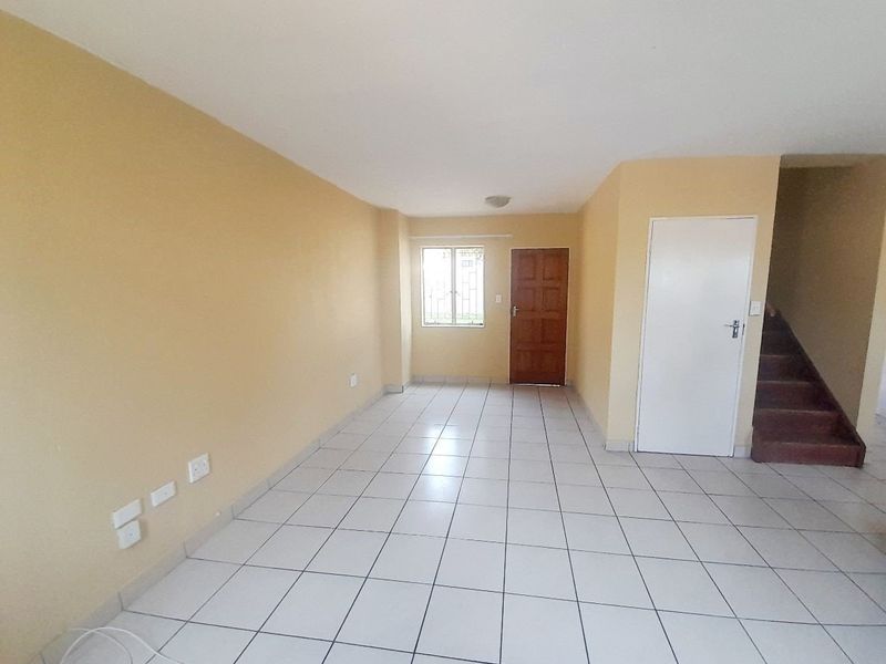 An empty, open-plan living area featuring neutral tiled flooring, a staircase, and a security gate, offering a blank canvas for personalization.