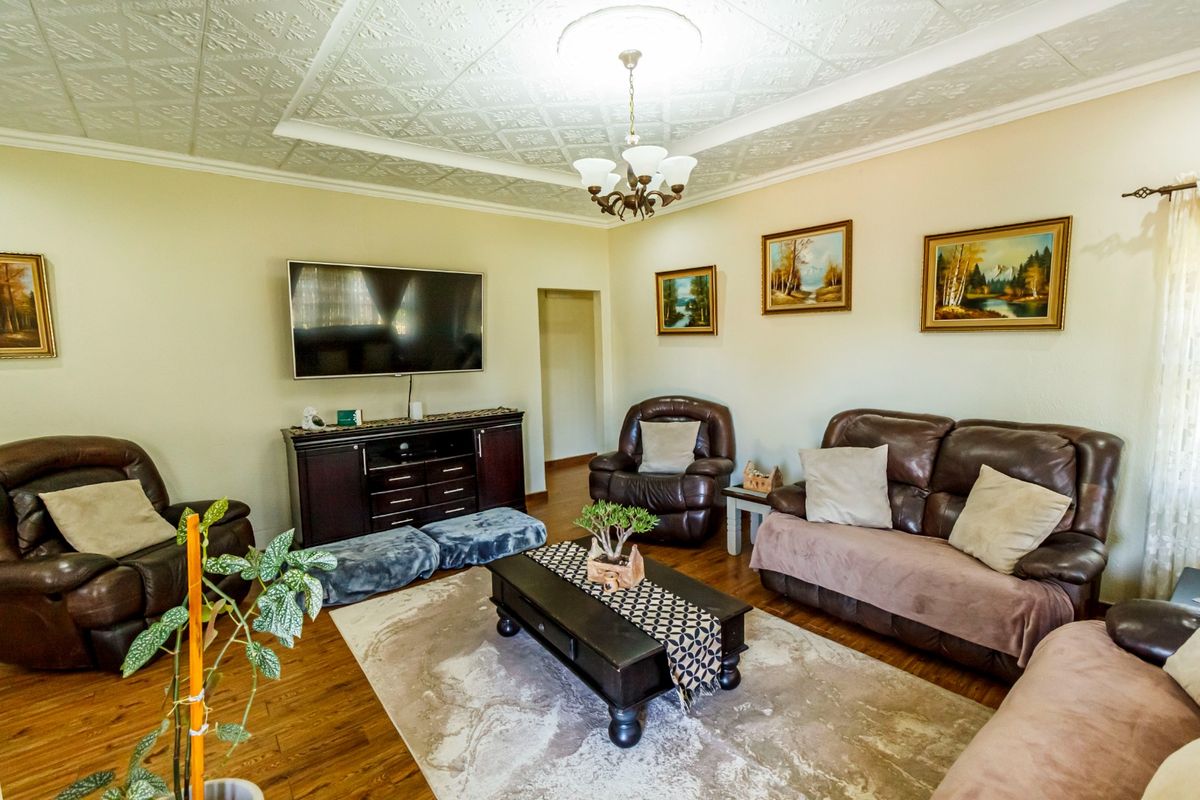 A comfortable living room featuring hardwood flooring, decorative ceiling tiles, and a central chandelier, providing a warm and inviting atmosphere.