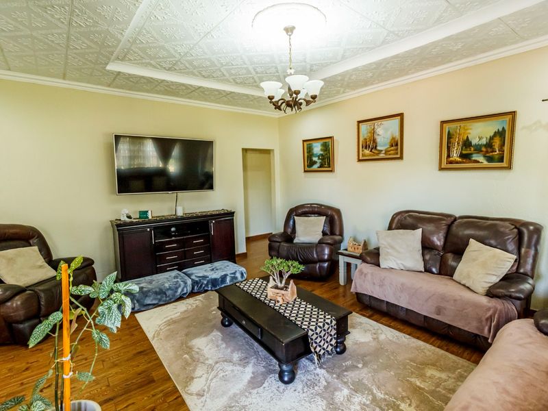 A comfortable living room featuring hardwood flooring, decorative ceiling tiles, and a central chandelier, providing a warm and inviting atmosphere.