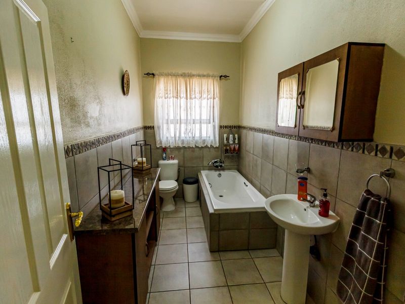 A functional bathroom featuring a pedestal basin, built-in bathtub, toilet, and tiled finishes, requiring some cosmetic attention to the wall surfaces.