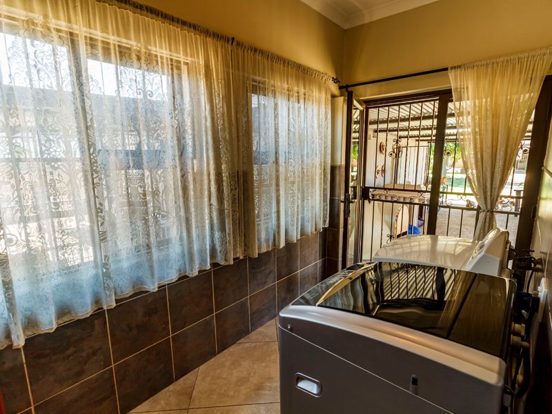 A functional laundry room featuring tiled walls and flooring, with direct access to an outdoor area through a security gate and sliding door.