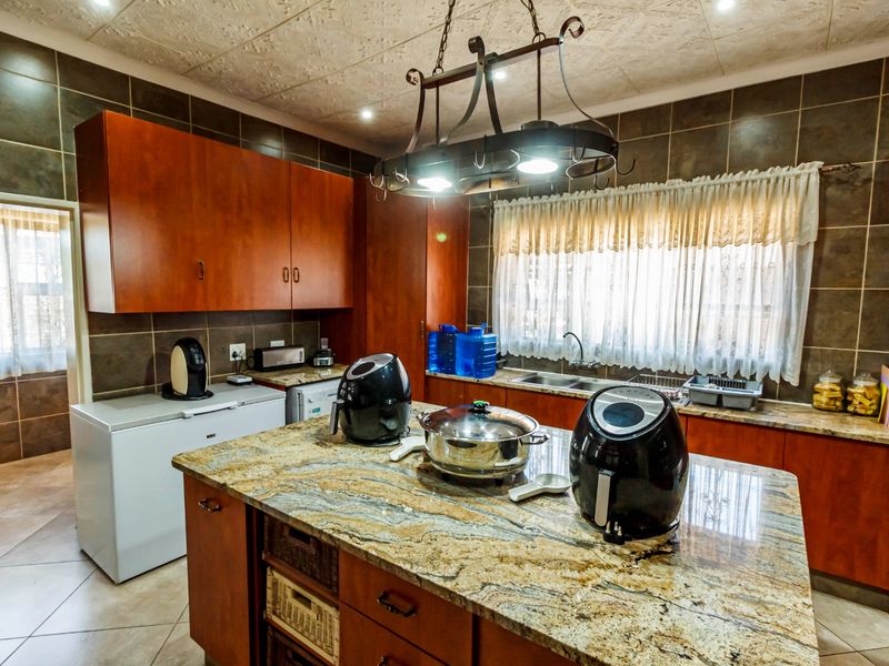 A spacious kitchen featuring warm-toned wooden cabinetry, granite countertops, a central island, and tiled finishes throughout.