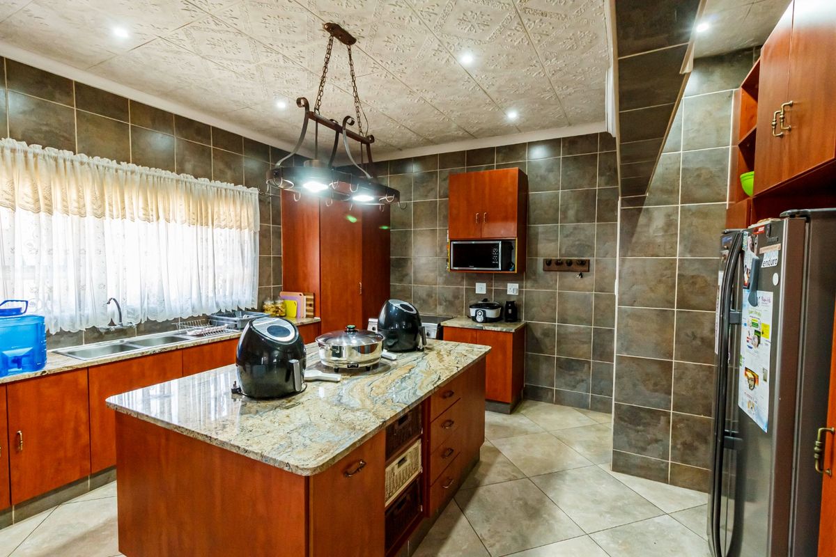 A spacious kitchen featuring granite countertops, a central island, extensive built-in cabinetry, and full-height wall tiling.