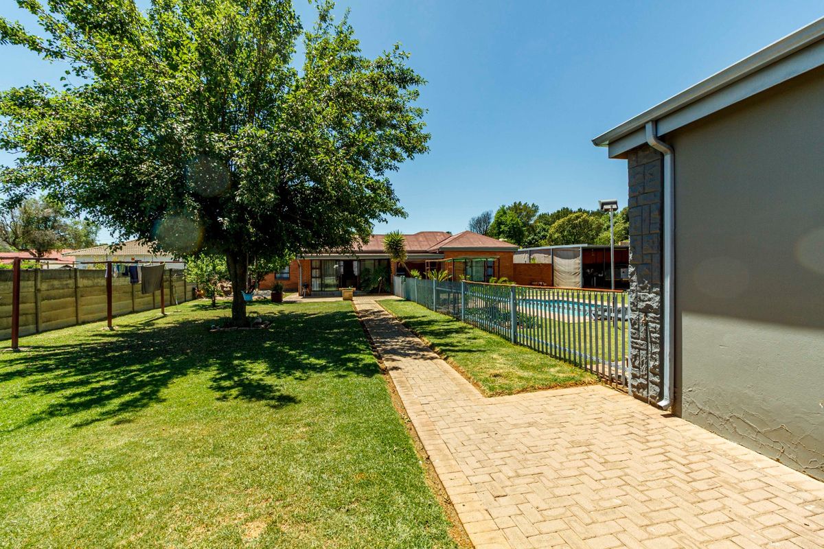 Spacious rear garden featuring a paved walkway, established tree, and a fenced swimming pool area adjacent to the main house structure.