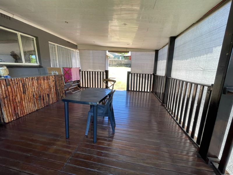 Covered patio area featuring timber decking, a built-in bar counter, and protective outdoor roller blinds, providing a functional space for outdoor entertainment.