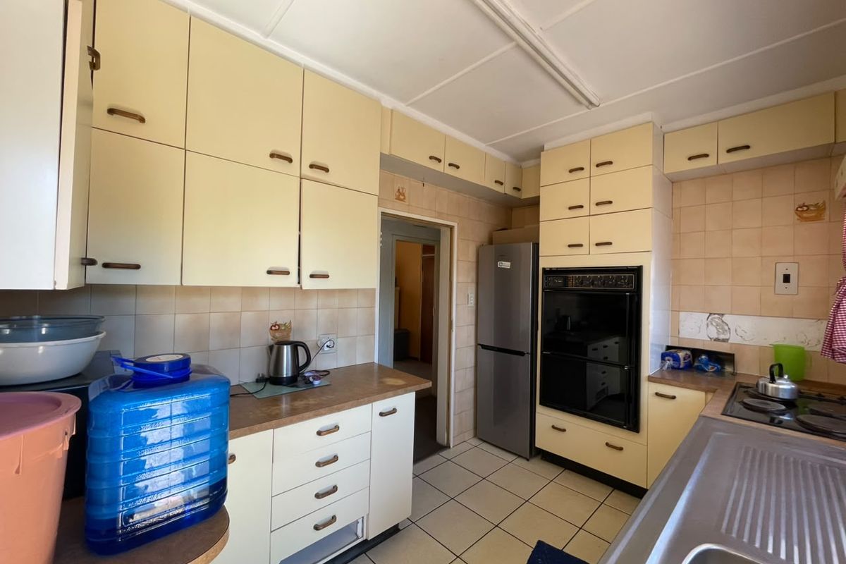 A functional kitchen featuring dated cabinetry, tiled backsplash, built-in oven, hob, and tiled flooring, offering potential for modernization.