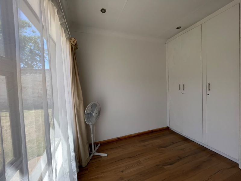 A bright, empty bedroom featuring laminate flooring, built-in cupboards, and a sliding door providing access to the garden.