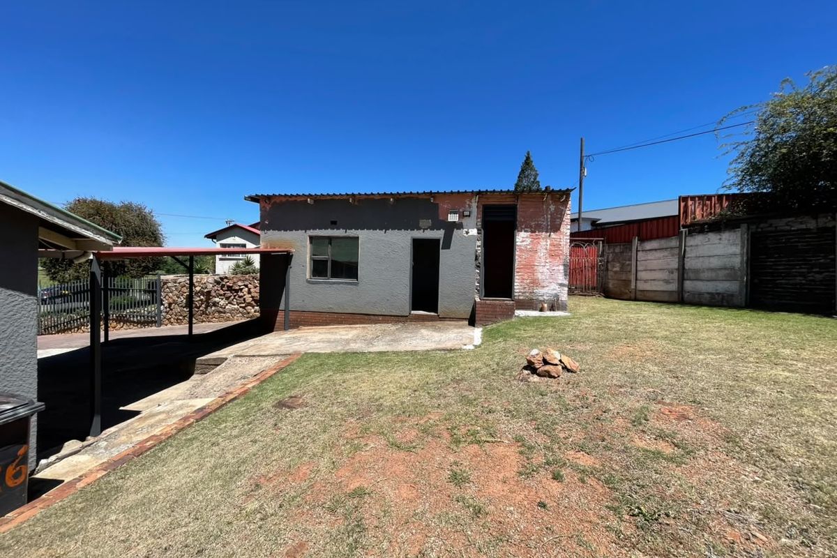 Rear view of the property featuring a concrete patio, attached carport, and a large backyard area with perimeter walling.