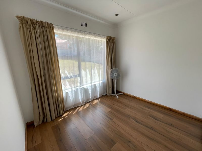 A bright and spacious bedroom featuring modern laminate flooring, neutral walls, and a large window that allows for plenty of natural light.