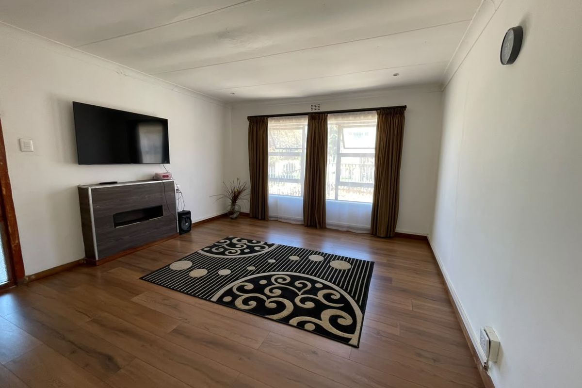 A living room featuring laminate flooring, coved ceilings, and large windows with curtains, providing a neutral space ready for personalization.