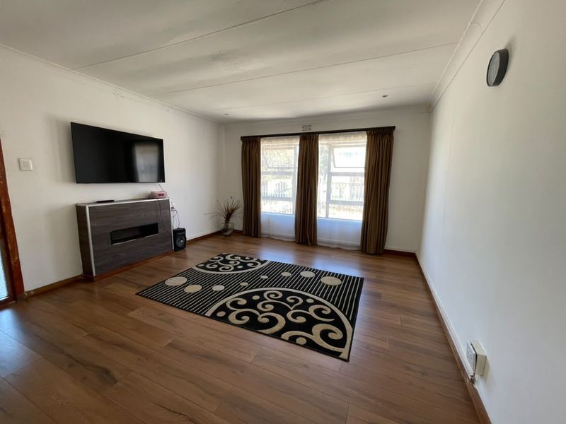 A living room featuring laminate flooring, coved ceilings, and large windows with curtains, providing a neutral space ready for personalization.