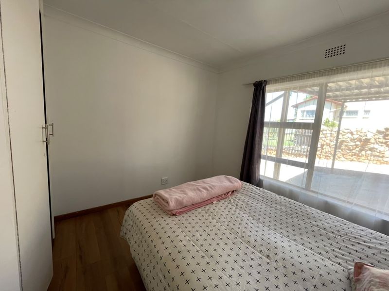A functional bedroom featuring laminate flooring, a built-in wardrobe, and a large window providing natural light.