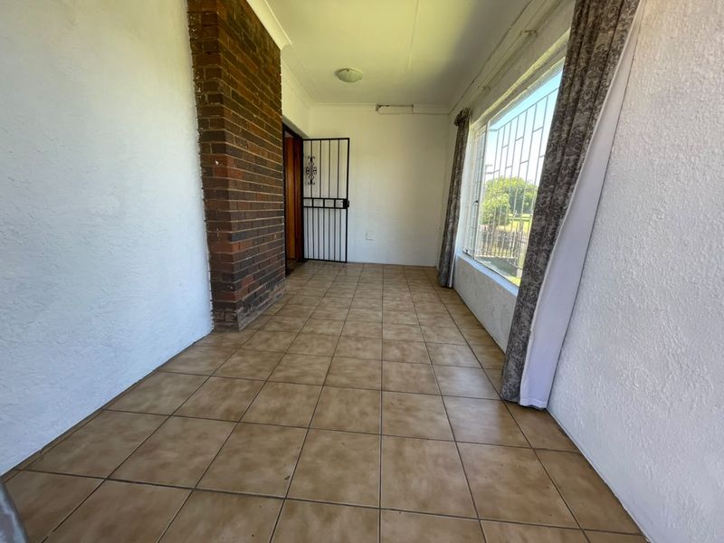 A covered patio area featuring tiled flooring, an exposed brick chimney, and security fixtures, offering a blank canvas for outdoor living space enhancement.