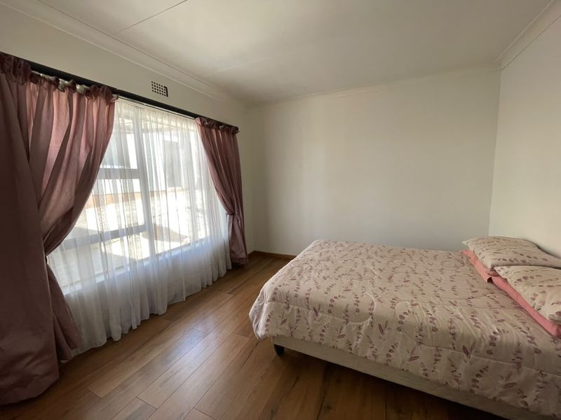 A bright bedroom featuring laminate flooring, neutral walls, and a large window with natural light, offering a clean and functional living space.