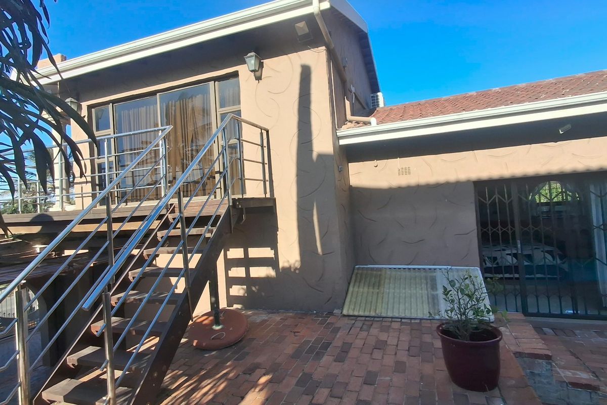 Rear exterior view featuring a brick patio, stainless steel staircase leading to an upper level, and sliding glass doors with security gates.