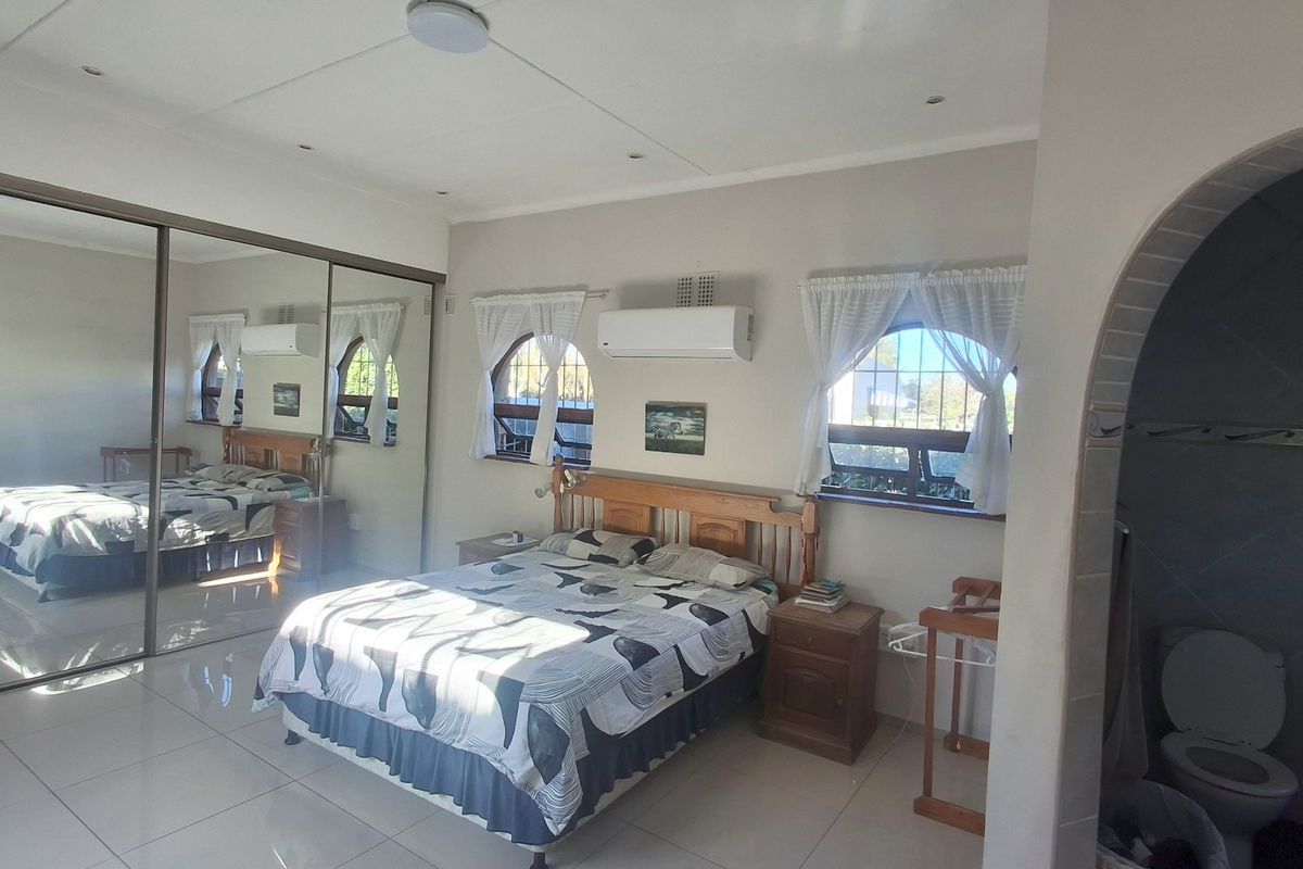 Spacious bedroom featuring tiled flooring, large mirrored sliding wardrobes, split-system air conditioning, and distinctive arched windows allowing for natural light.