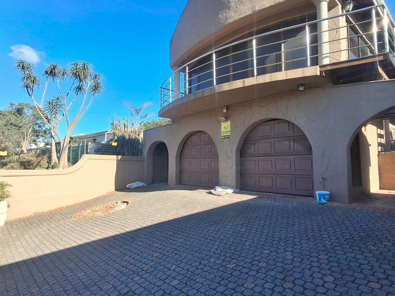 Front elevation of a multi-story house featuring a double garage with arched openings, a paved driveway, and an upper-level balcony with stainless steel railings.