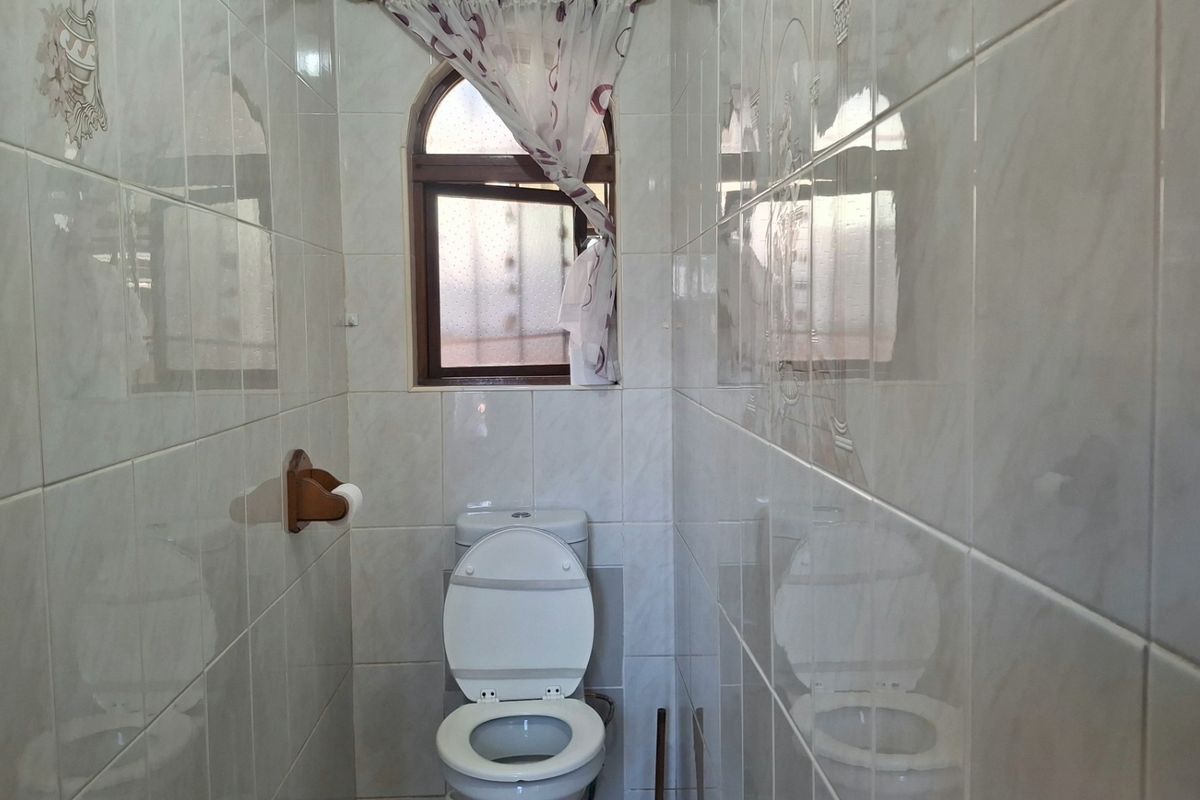 A compact bathroom featuring full-height ceramic wall tiling and an arched window, providing a functional and clean space.
