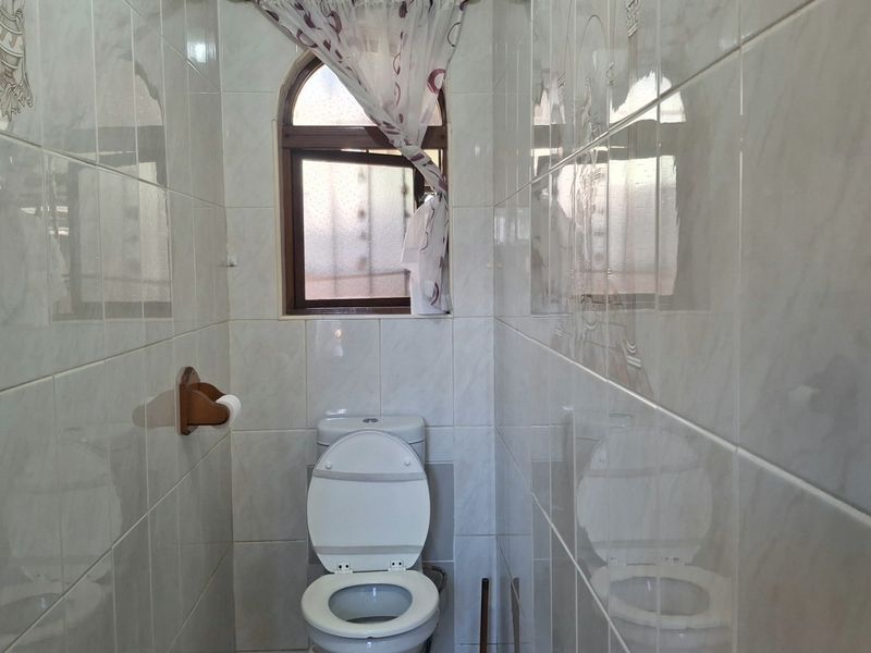 A compact bathroom featuring full-height ceramic wall tiling and an arched window, providing a functional and clean space.
