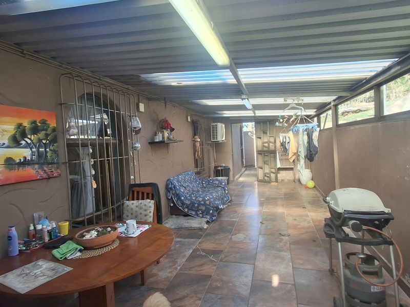 A covered outdoor patio area featuring tiled flooring, corrugated roofing, and security bars, providing a functional space for outdoor living and entertainment.