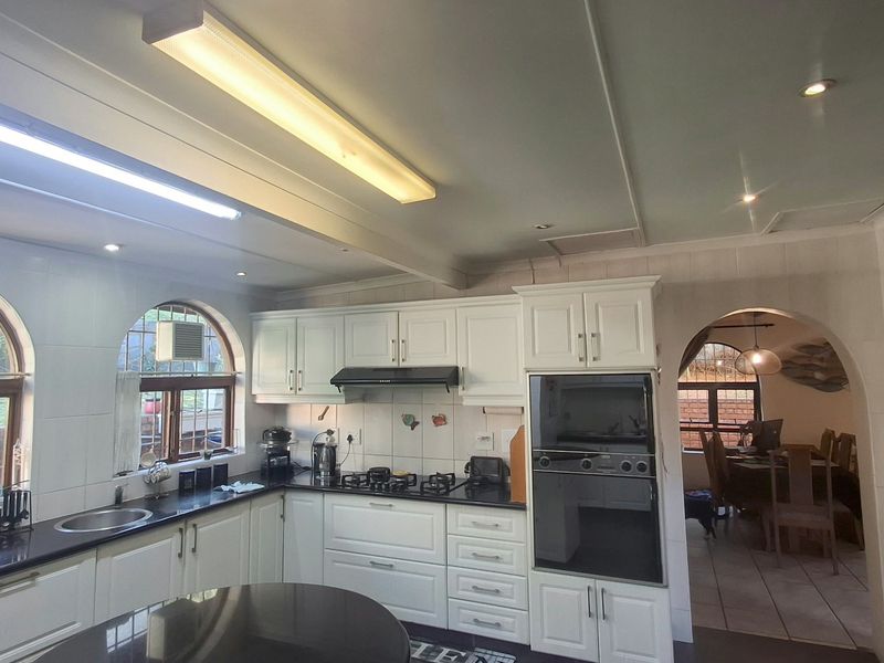 A well-appointed kitchen featuring white cabinetry, granite countertops, built-in oven, gas hob, and distinctive arched windows, offering a functional and classic design.
