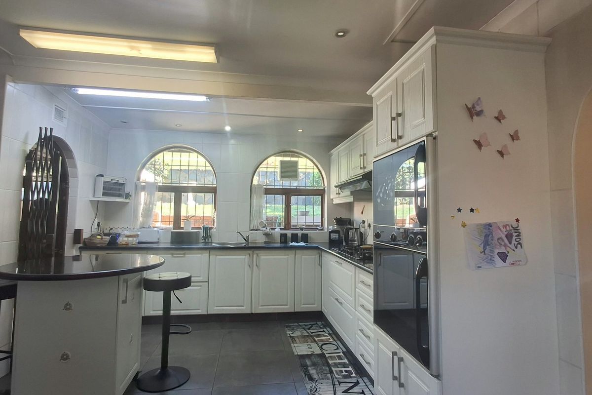A functional kitchen featuring white cabinetry, a double wall oven, integrated hob, breakfast bar, and arched windows providing natural light.