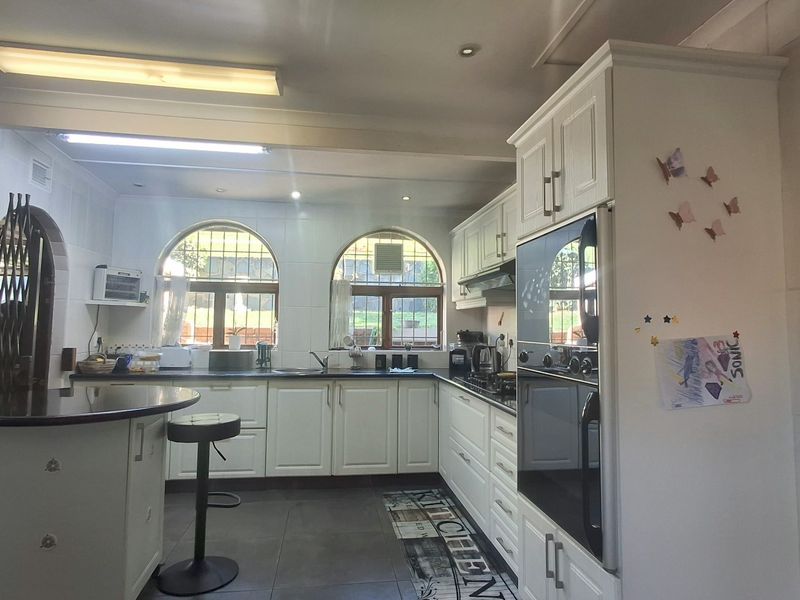 A functional kitchen featuring white cabinetry, a double wall oven, integrated hob, breakfast bar, and arched windows providing natural light.
