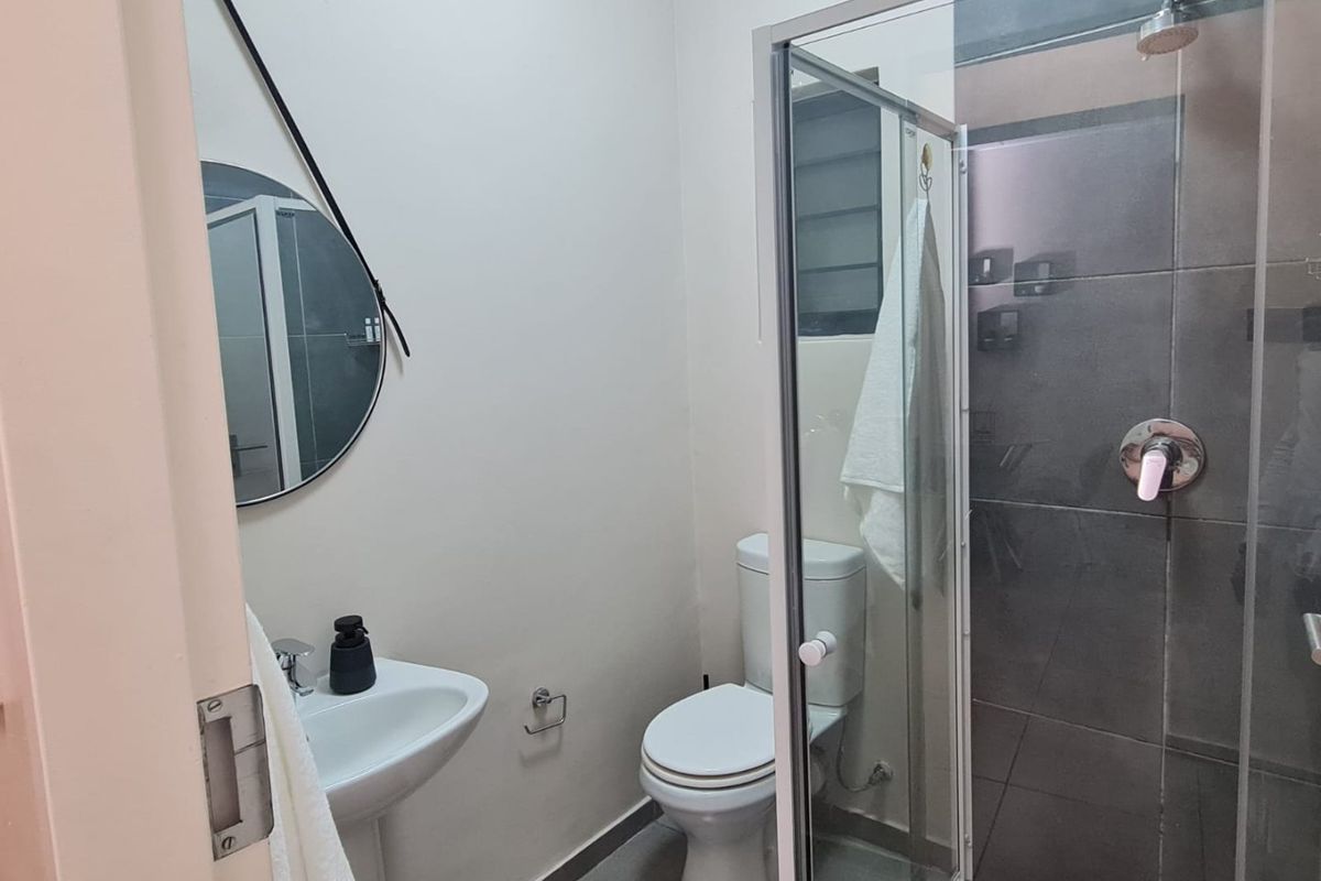 A compact, modern bathroom featuring a pedestal basin, a toilet, and a glass-enclosed shower with dark grey wall tiling.