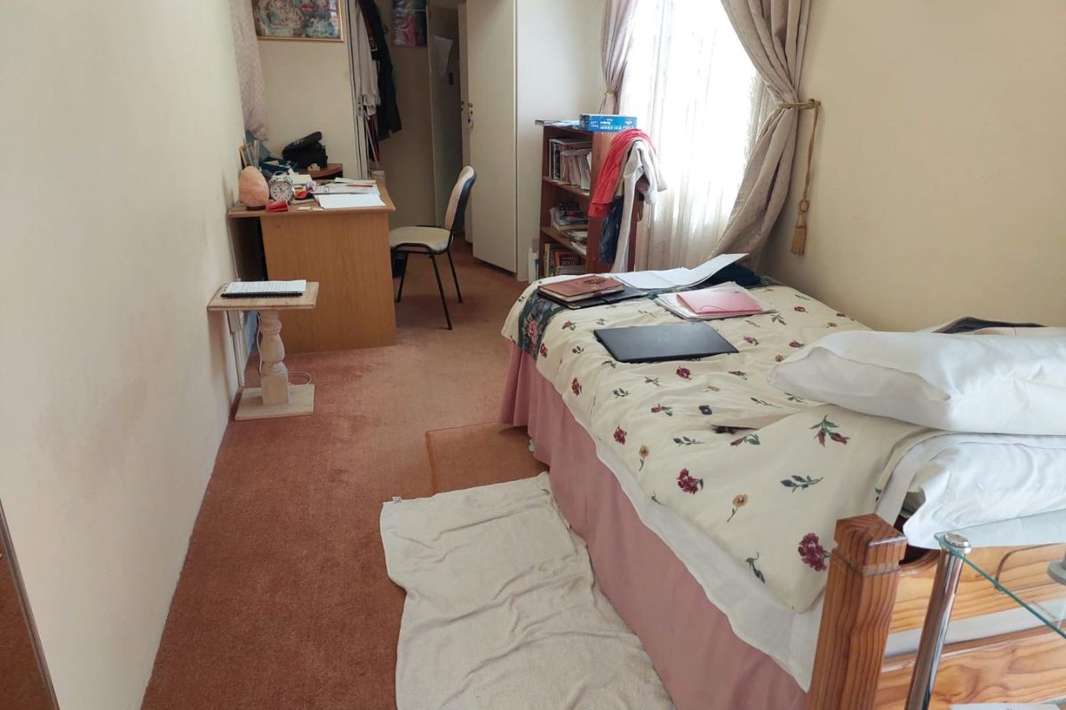 A compact bedroom featuring carpeted flooring and natural light from a window, offering a functional space that could benefit from cosmetic updates.