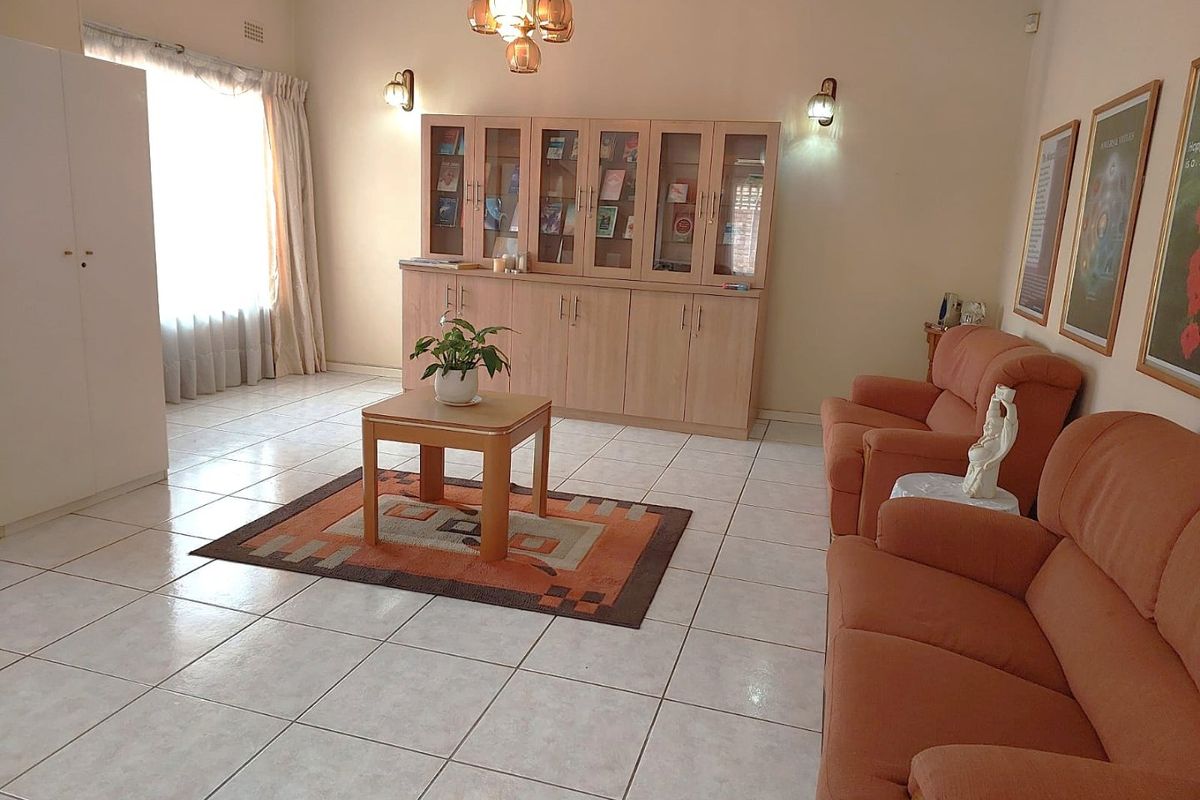 A spacious living area featuring neutral tiled flooring, built-in wooden cabinetry, and warm wall-mounted lighting, offering a functional and well-maintained space.
