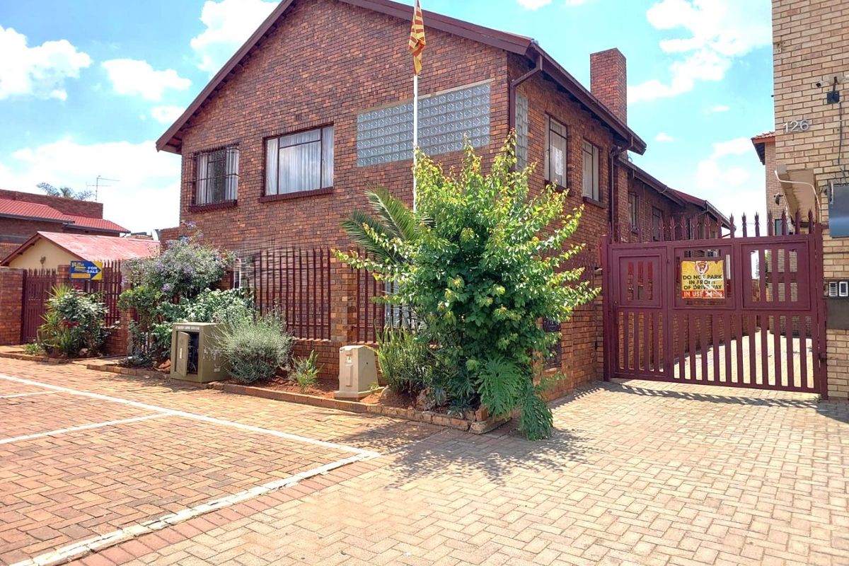 Front exterior view of a commercial brick building featuring a paved driveway, secure metal gate, and perimeter fencing.