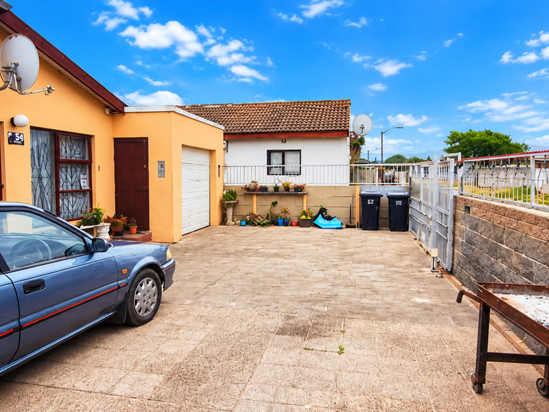 Front exterior view of the property featuring a paved driveway, secure boundary wall, and garage access.