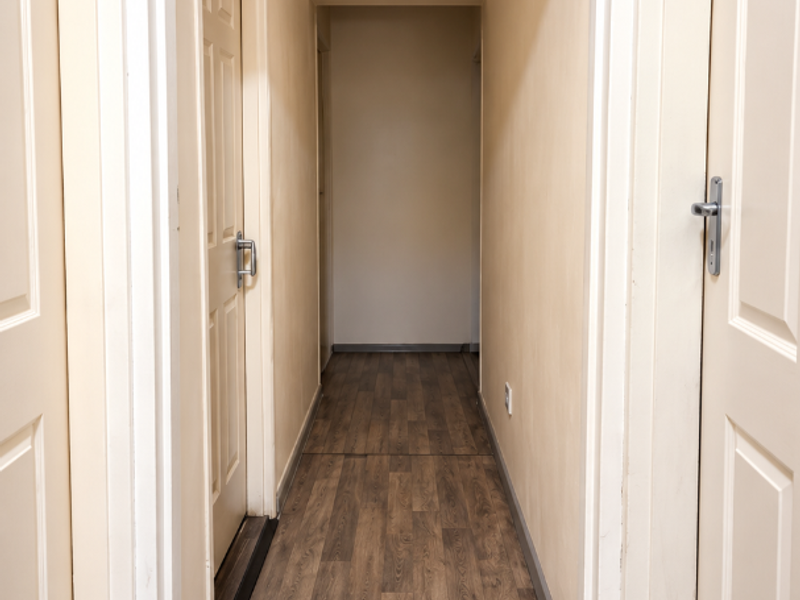 A clean, empty hallway featuring a transition between tiled and laminate flooring, with neutral walls and multiple internal doors.