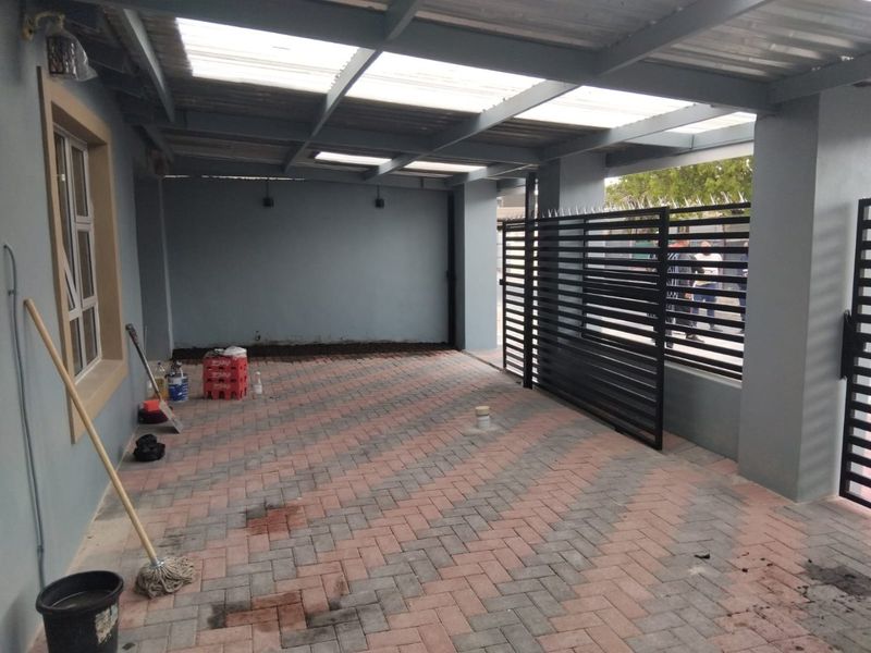 A covered outdoor patio area featuring paved flooring and a secure metal gate, suitable for use as a carport or entertainment space.