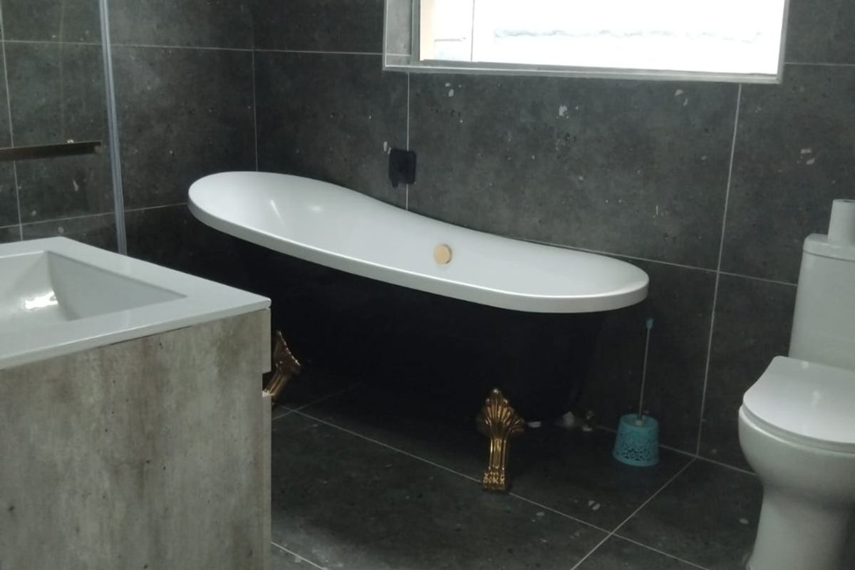 A bathroom featuring a black clawfoot bathtub, wall-mounted vanity, and grey tiled finishes throughout, providing a modern yet classic aesthetic.