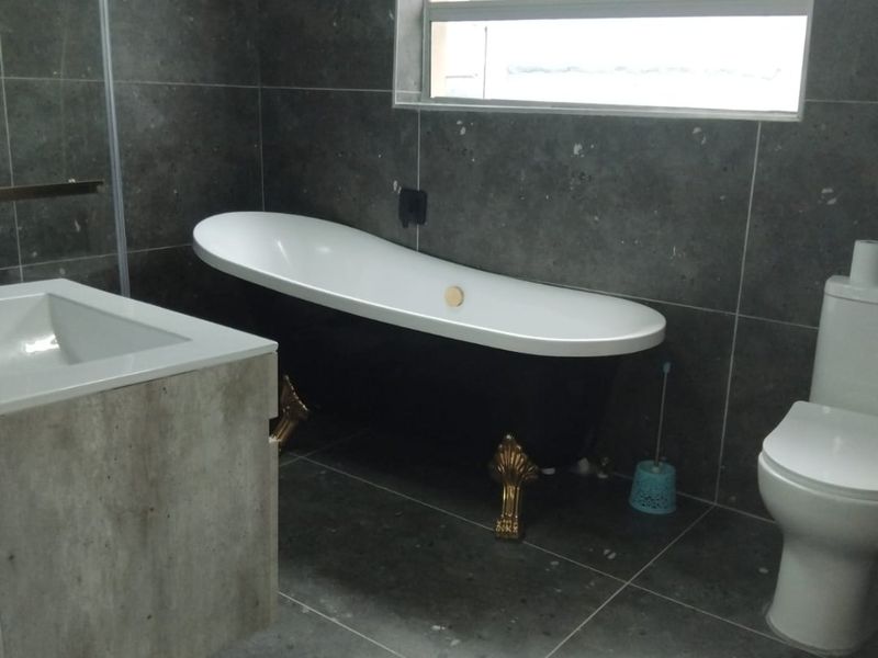 A bathroom featuring a black clawfoot bathtub, wall-mounted vanity, and grey tiled finishes throughout, providing a modern yet classic aesthetic.