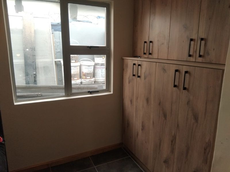 A clean and functional scullery area featuring modern wood-look built-in cabinetry and tiled flooring, providing ample storage space.
