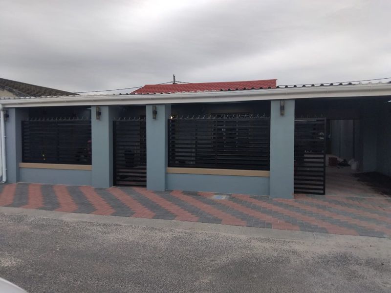 Front elevation featuring a paved driveway, secure boundary wall with metal gates, and a covered carport area.