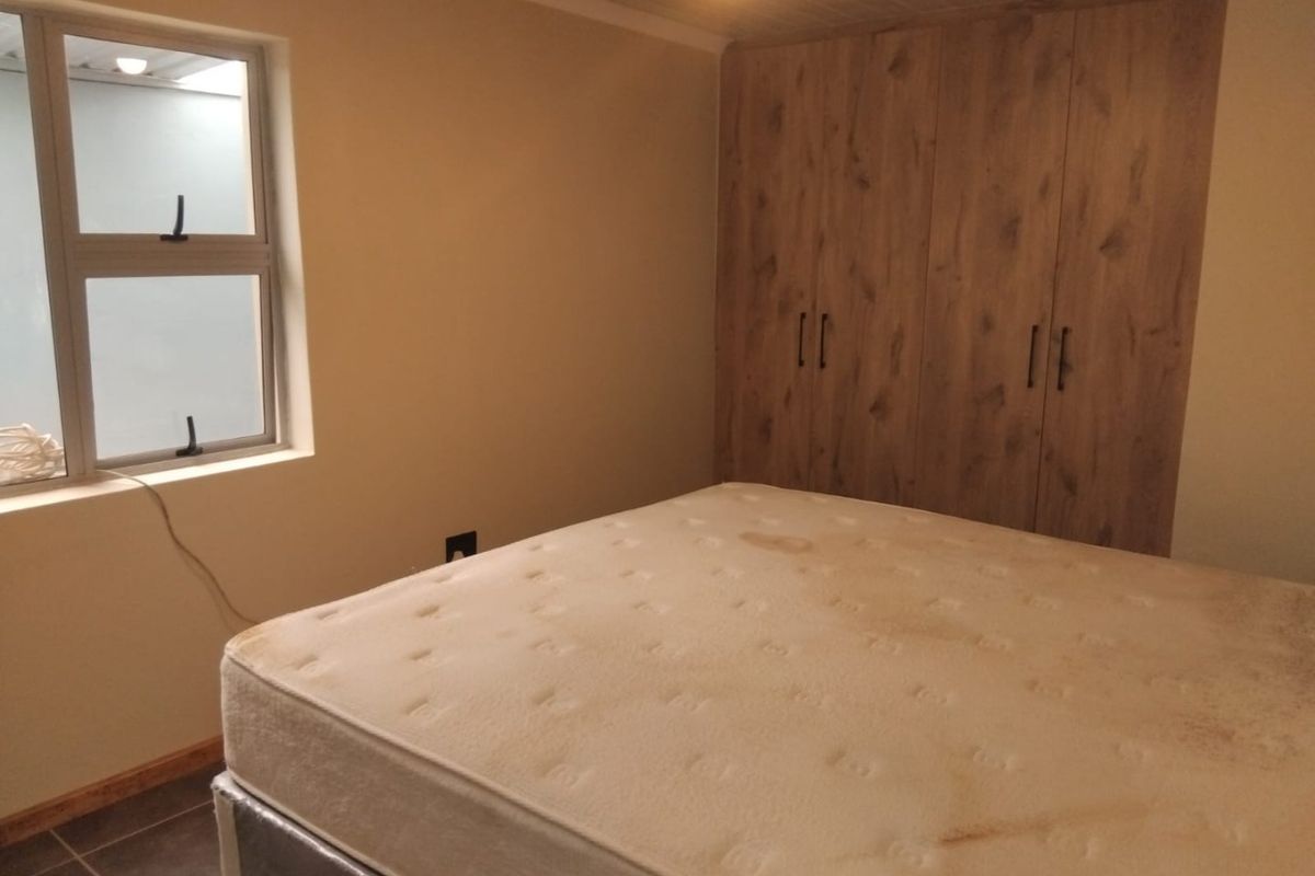 A bedroom featuring built-in wooden cupboards, tiled flooring, and an aluminium window frame, providing a functional and neutral living space.
