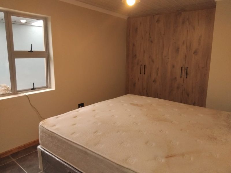 A bedroom featuring built-in wooden cupboards, tiled flooring, and an aluminium window frame, providing a functional and neutral living space.